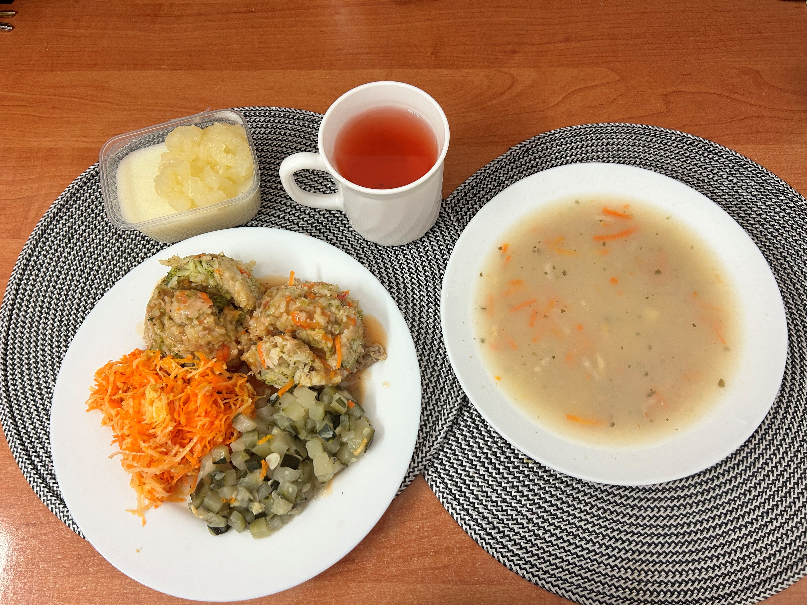 Na zdjęciu znajduje się: Barszcz biały z ziemniakami, Risotto z mięsem wieprzowym i warzywami, Sos pomidorowy, Cukinia pieczona z olejem, Surówka z selera i marchwi z olejem, Kompot owocowy, Kasza manna z jabłkiem prażonym